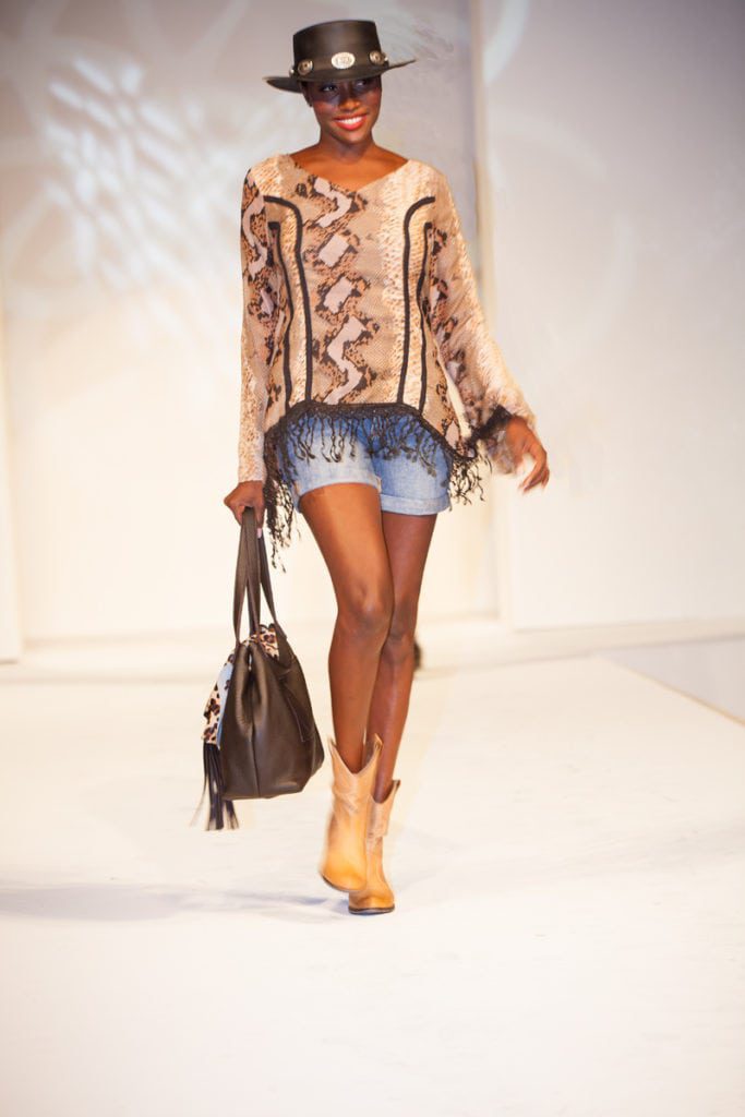 A woman walking down the runway with a brown bag