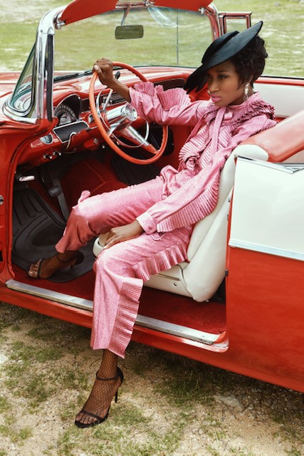 A woman wearing a pink suit and sitting in a red car