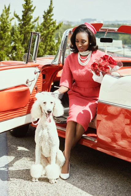 A woman wearing a pink dress and posing with a poodle